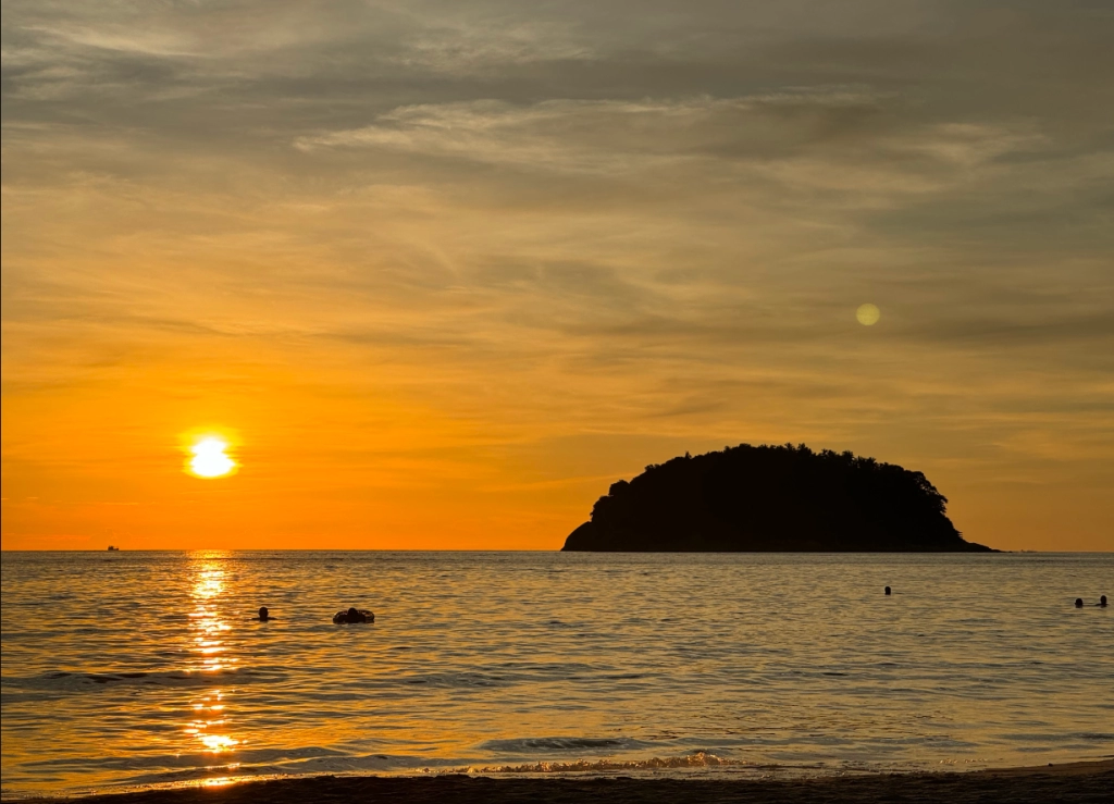 💰 Investing Guides | Phuket vs Bali vs Vietnam – Where to Invest? Sunset over Kata Beach in Phuket with silhouettes of swimmers and a coastal island, featured in Phuket vs Bali vs Vietnam investment guide.