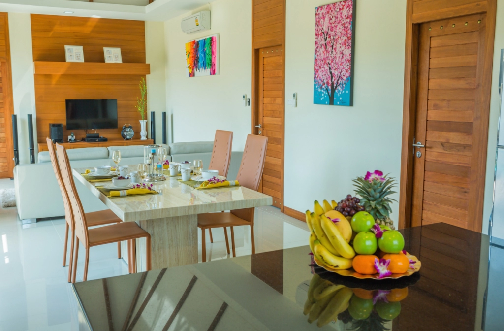 Modern furnished condo interior in Thailand with dining table, sofa, and tropical fruit on kitchen counter