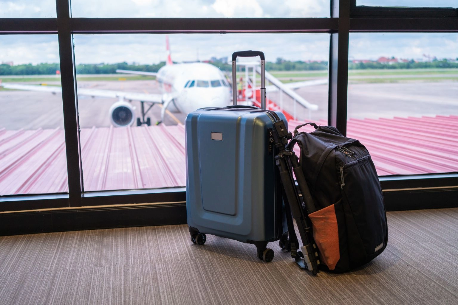 Suitcase and backpack at airport window with airplane, representing travel demand and Airbnb pricing strategy timing